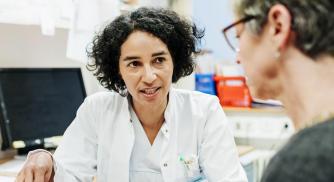 An image of a doctor in a white coat reviewing information on a tablet with a woman