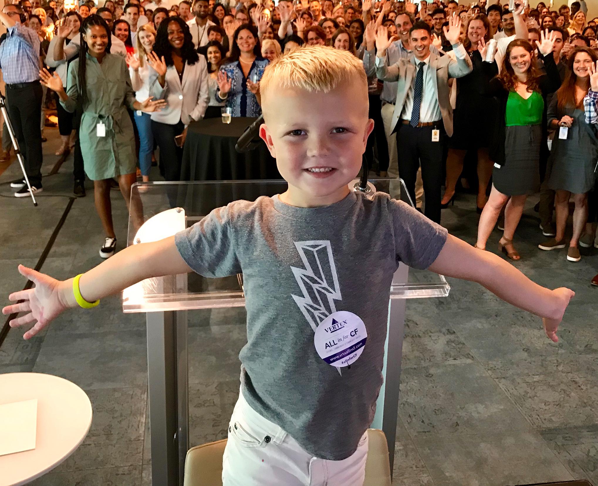 Image of a young boy with CF standing in front of a group of Vertex employees
