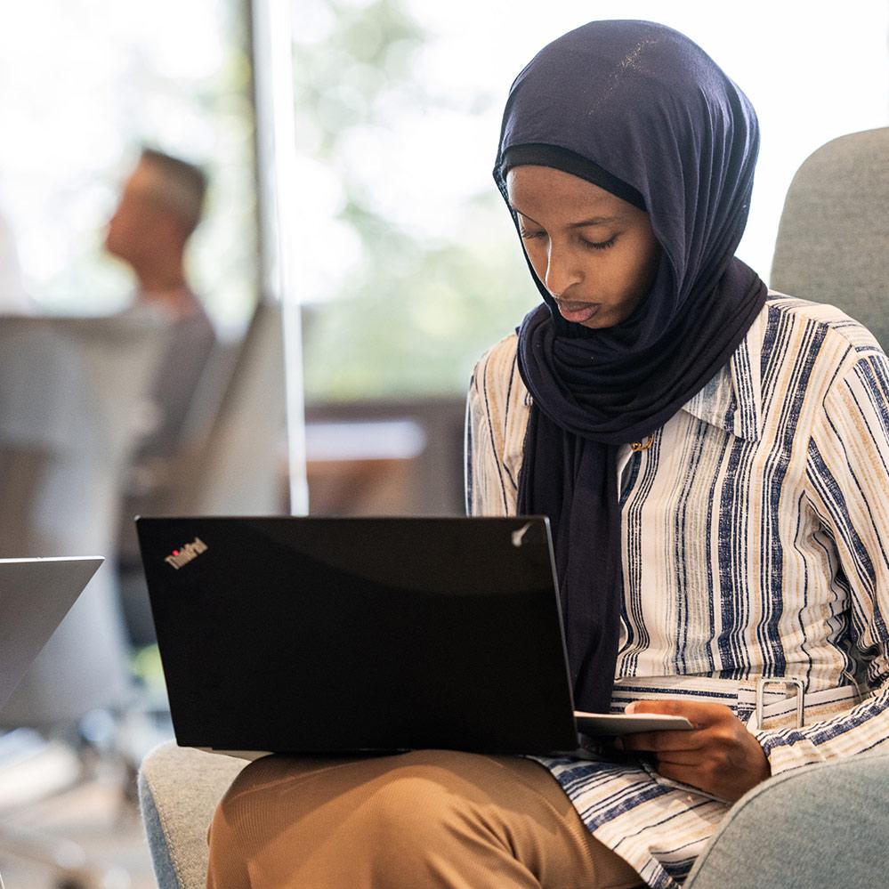 An image of a female high school intern at Vertex Pharmaceuticals' San Diego Research Site. She is sitting in a chair and looking at a laptop. 