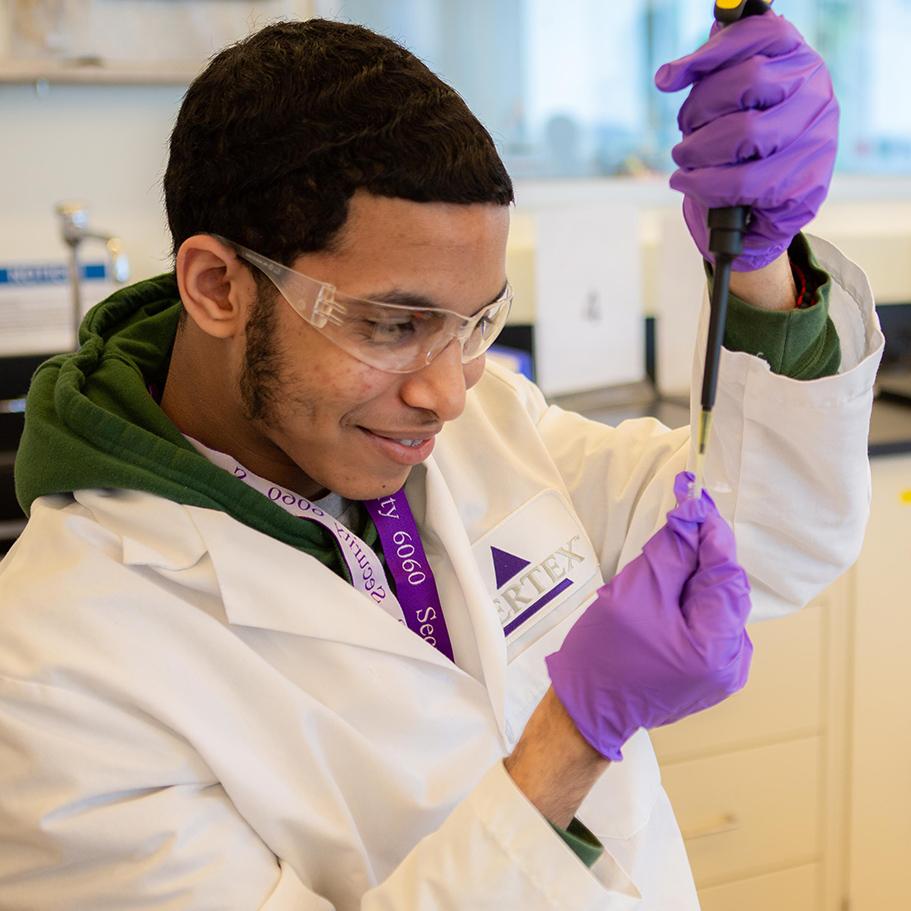 A teenage male science student wearing a Vertex lab coat uses a pipette