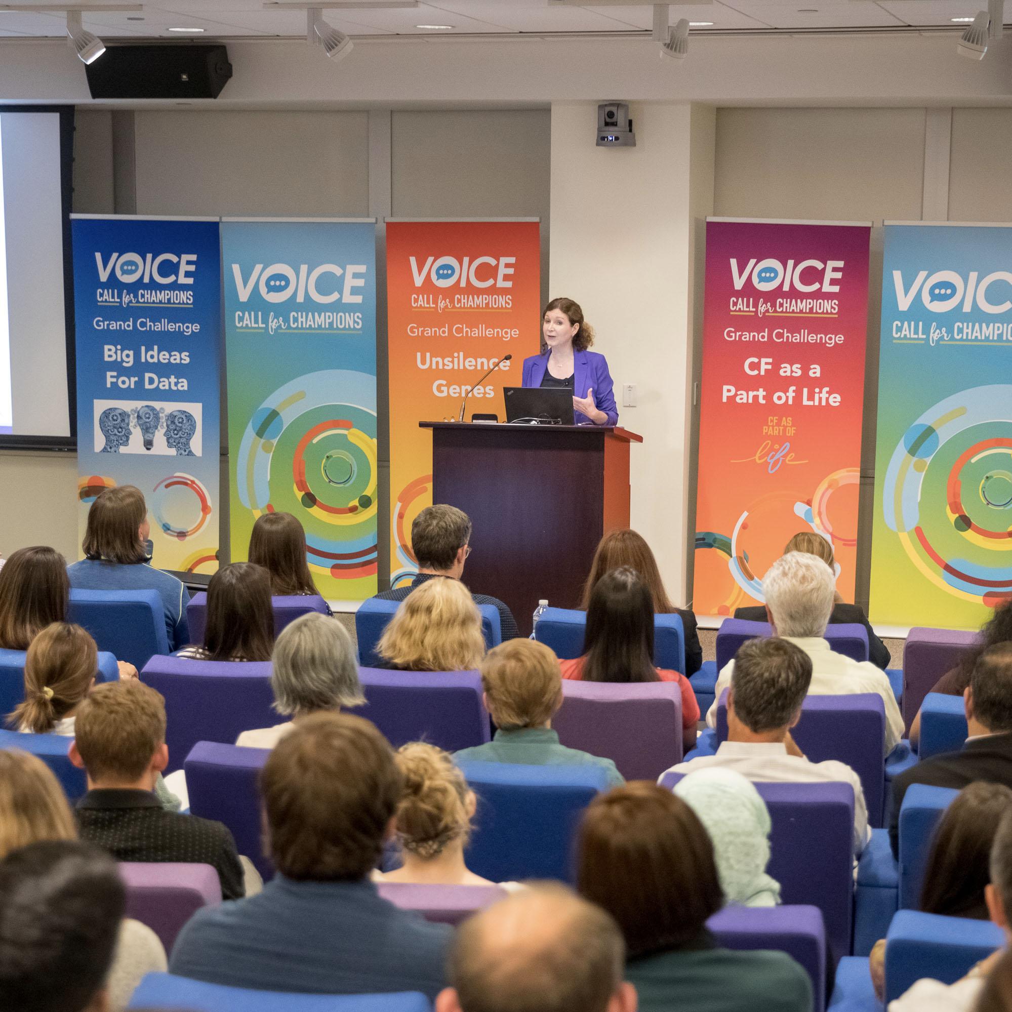 A woman presents in the Vertex Pharmaceuticals auditorium during the VOICE program