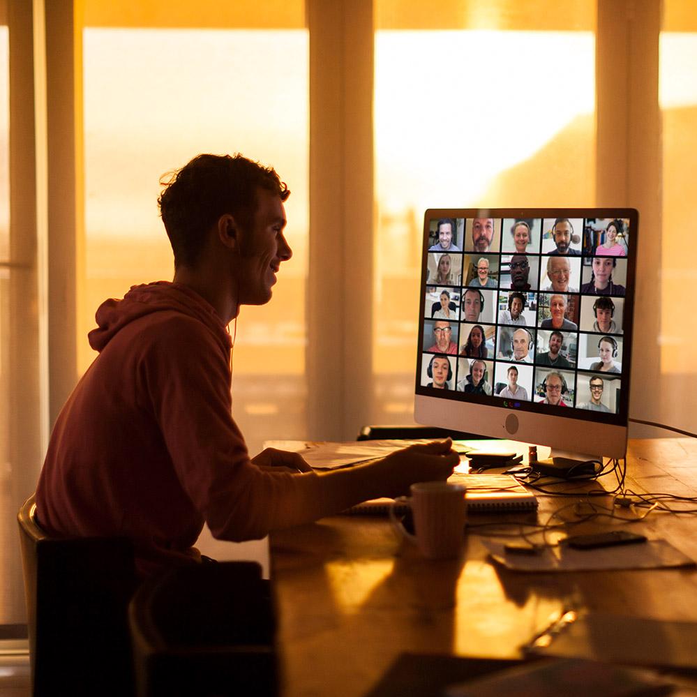 A photo of a man sitting at a computer attending a Zoom meeting