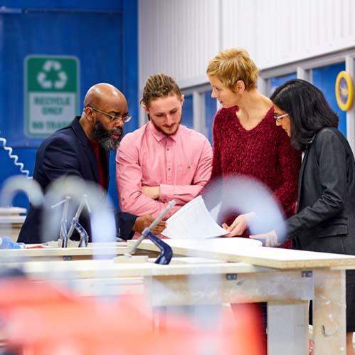 An image of 4 people huddled together reviewing items on a table