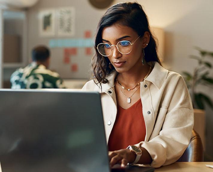 An image of a woman sitting at a desk while using a laptop
